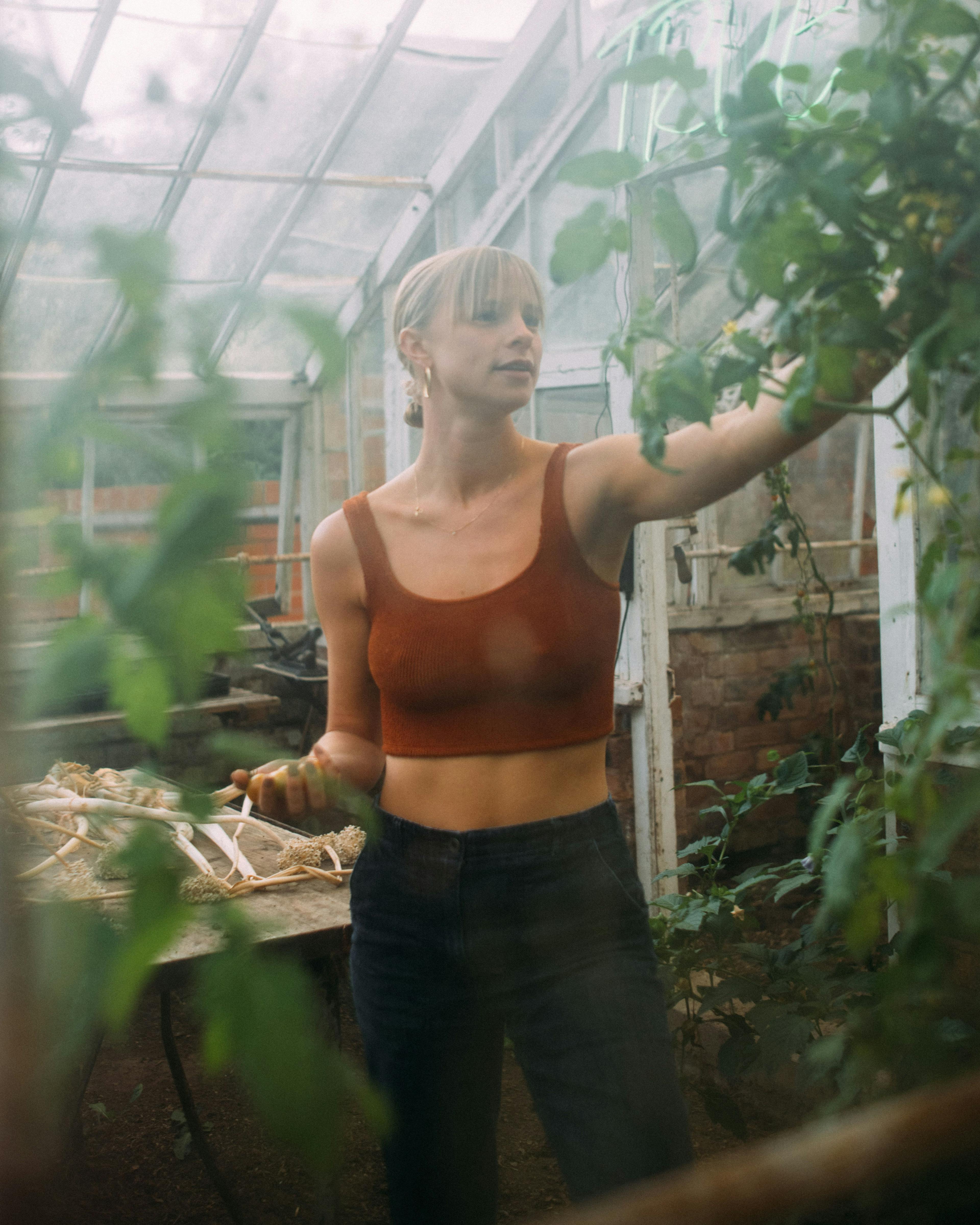 Xanthe in greenhouse picking fruit in bikini top and jeans