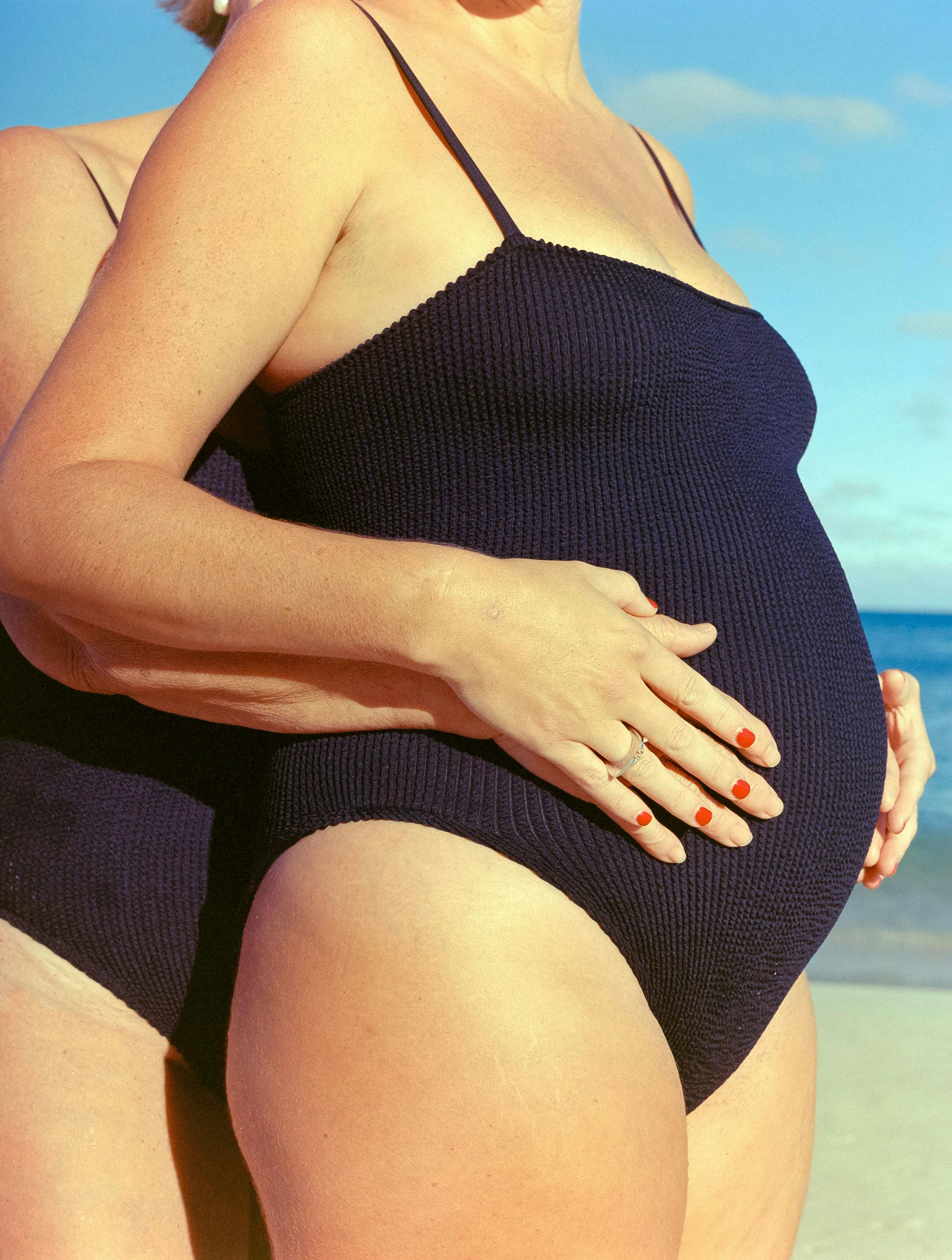 Elise with pregnancy bump wearing black swimsuit